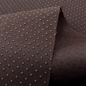 May include: Close-up of brown fabric with a textured surface. The fabric has a pattern of small, evenly spaced dots.