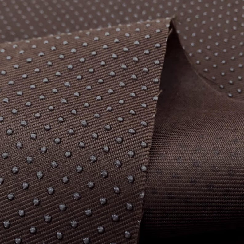 May include: Close-up of brown fabric with a textured surface. The fabric has a pattern of small, evenly spaced dots.