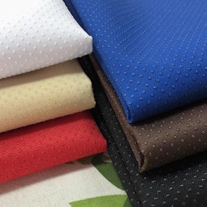 May include: A stack of five fabric swatches in different colors, including white, beige, red, brown, and blue. Each swatch has a textured surface with small raised dots.