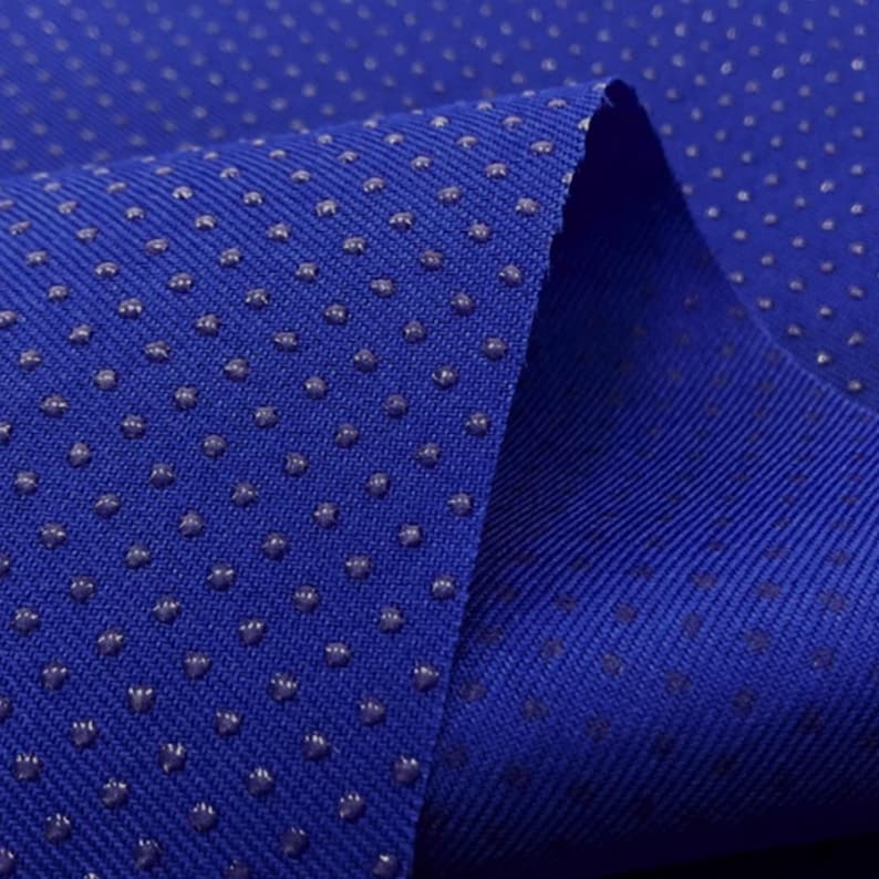 May include: Close-up of a blue fabric with a textured surface. The fabric has small, raised dots that create a subtle pattern.