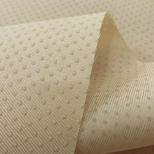 May include: Close-up of a beige fabric with a textured surface. The fabric has a pattern of small dots.