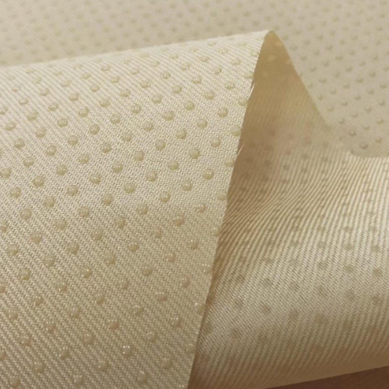 May include: Close-up of a beige fabric with a textured surface. The fabric has a pattern of small dots.