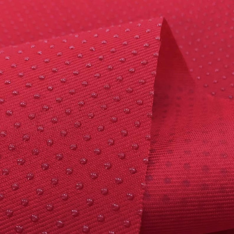 May include: Red fabric with a textured surface. The fabric has small, raised dots that create a subtle pattern.