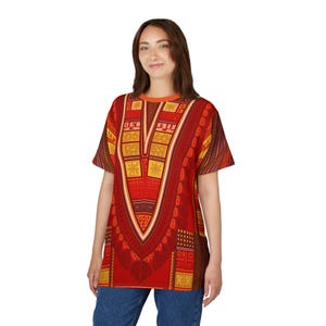 May include: A red and yellow patterned tunic-style shirt with short sleeves. The shirt features a V-neck design with geometric and floral patterns. The model is wearing blue jeans.