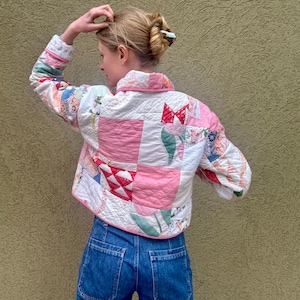 May include: A quilted jacket with a patchwork design in shades of pink, white, and other colors. The jacket has a cropped fit, a collar, and long sleeves. The jacket is paired with blue denim jeans.