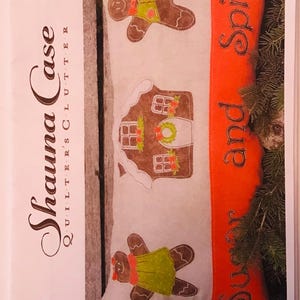 May include: A white pillow with a gingerbread house, gingerbread person, and the text "Sugar and Spice" in black on a red background. The pillow is part of a quilting pattern called "Sugar and Spice - Pillow QC406-17".