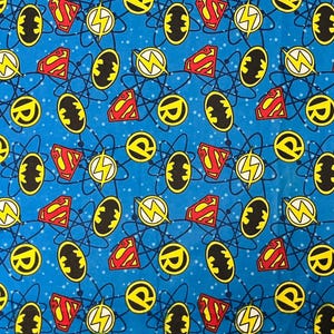 May include: Blue fabric with a repeating pattern of superhero logos, including Superman's 'S' shield, Batman's bat symbol, the Flash's lightning bolt, and Robin's 'R'. The logos are in red, yellow, and black, connected by blue lines and white dots.