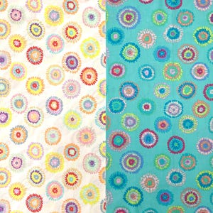 May include: Two fabric samples, one white and one teal, feature a repeating pattern of colourful, stylised floral designs. The flowers are made up of concentric circles in shades of yellow, orange, red, purple, and blue.