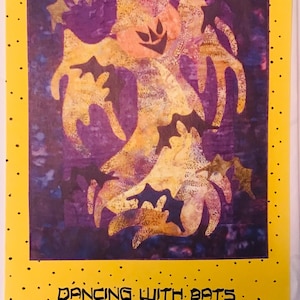 May include: A quilt pattern for a wall hanging featuring a purple background with a yellow and black silhouette of a dancing figure with bats. The text "Dancing With Bats 20-1/2 x 24-1/2 Wall Hanging" is printed below the image.