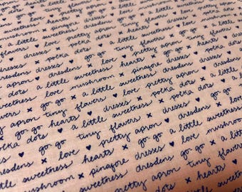 May include: Close-up of a fabric with a light pink background. The fabric is covered in a repeating pattern of handwritten words and phrases in dark blue, including "love," "hearts," and "flowers."