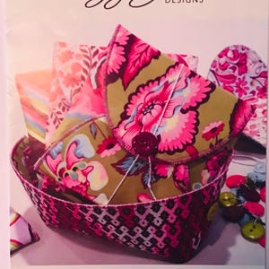 May include: A pink and green fabric gift wrap with a floral pattern. The wrap is folded into a small envelope shape and is sitting in a pink and black basket. The text "PREZZIES" is at the bottom of the image. The text "Lazy Girl Designs" is at the top of the image. The text "LGD139" is in the top right corner of the image.