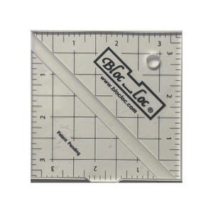 May include: A clear, square quilting ruler with grid lines and diagonal markings. The ruler features the text "Bloc Loc" and "www.blocloc.com". The words "Patent Pending" are also visible. A small, clear ring is also present.