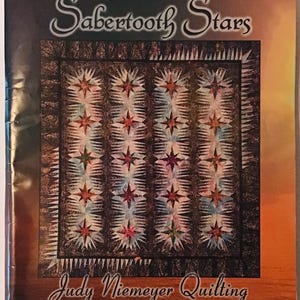 May include: A quilt pattern for a quilt called "Sabertooth Stars" by Judy Niemeyer Quilting. The pattern is for a quilt that is 76 inches by 90 inches. The quilt pattern features a design of stars with a sabertooth shape.