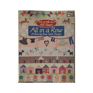 May include: A colorful quilt book cover with the title "All in a Row" and the text "24 Row-by-Row Quilt Designs." The cover features various quilt block designs, including houses, flowers, and geometric patterns. The Moda All-Stars logo is also visible.