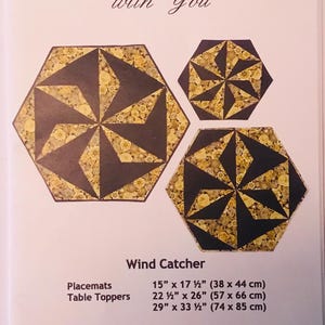 May include: Three hexagon-shaped quilted table toppers in a "Wind Catcher" pattern. The largest topper is 29 inches by 33 1/2 inches, the middle topper is 22 1/2 inches by 26 inches, and the smallest topper is 15 inches by 17 1/2 inches. The pattern features a black and gold color scheme with a floral print.