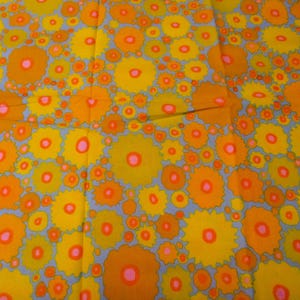 May include: A fabric with a repeating pattern of orange and yellow flowers with pink centres on a light blue background.