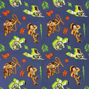 May include: Navy blue fabric with a repeating pattern of cartoon characters. The design includes a space ranger in a green and white spacesuit, a cowboy, a horse, and other themed elements in orange, green, and brown.