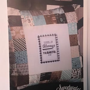 May include: A brown and white patchwork pillow with a black and white checkered label that says "There is always something to be thankful for". The pillow is labeled "Sweetwater Mini Charm Pillow".