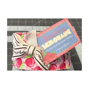 May include: A fabric bundle tied with a cream and black striped ribbon bow. The pink fabric features a strawberry design. A tag reads "Strawberry Lemonade" and "by Me and My Sister Designs moda".