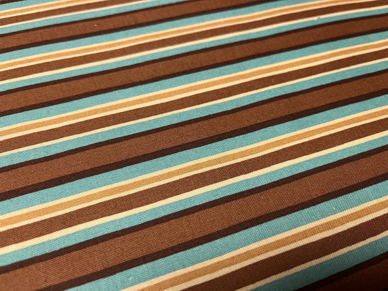 May include: Close-up of a fabric with a striped pattern. The stripes alternate between shades of brown, light blue, beige, and white. The fabric has a textured appearance, and the stripes run diagonally across the image.
