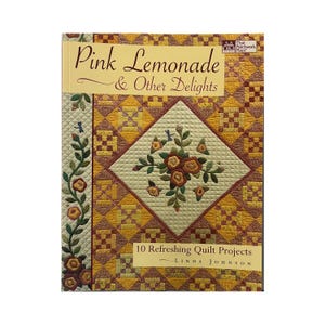 May include: A book titled "Pink Lemonade & Other Delights" featuring 10 quilt projects. The cover displays a patchwork quilt design with a central diamond showcasing floral embroidery in shades of brown, yellow, and green. The book's title is in elegant script.