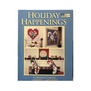 Peut inclure: Un livre bleu intitulé "Holiday Happenings" présentant des images de broderies sur le thème des fêtes. La couverture affiche un collage de projets de point de croix, dont un cœur avec des fleurs, un lapin, un Père Noël et des bas de Noël. Le nom de l'auteur, Christal Carter, est également visible.