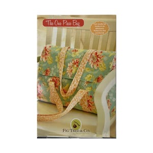 May include: A floral print bag with a light green background and red and yellow flowers. The bag has a matching strap and the text "The One Piece Bag" is visible. The Fig Tree & Co. logo is also visible.