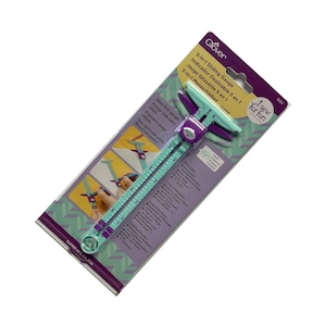 May include: A Clover 5-in-1 sliding gauge in a package. The gauge is teal and purple with a ruler marked in inches. The packaging includes text in multiple languages, including English and Spanish. The gauge is designed for sewing and quilting.