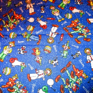 May include: A blue fabric with a repeating pattern of clowns, balls, and the words "BOOM" and "WOOD".