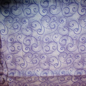 May include: A purple and white fabric with a repeating pattern of swirls. The fabric has a vintage, faded look.