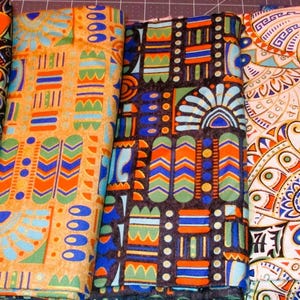 May include: Six fabric swatches with geometric patterns in shades of blue, orange, and gold. The patterns include stylized flowers, chevrons, and geometric shapes.