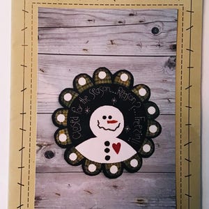 May include: A brown paper pattern for a penny rug featuring a snowman with the text "Closed for the Season... Reason? Freezin'" and the words "Wooden Spool Designs".
