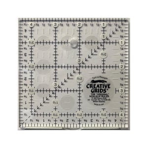 May include: A clear, square Creative Grids non-slip ruler with black markings and measurements in inches. The ruler features a grid pattern, circular cutouts, and the brand name. The text "Turn-a-Round" is also visible.