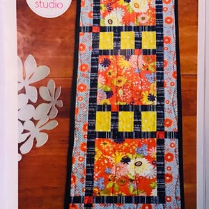 May include: A colorful table runner and place mat pattern with a floral design. The pattern is called "Anna Banana" and is from Pink Chalk Studio.