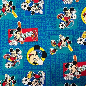 May include: A blue fabric with a repeating pattern of Mickey Mouse playing baseball and soccer. The fabric has the words "baseball", "soccer", and "all" repeated throughout.