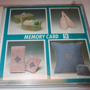May include: A clear plastic case containing a product display. The display features images of various items, including a tissue box, a basket, napkins, towels, a pillow, and a small pouch, all with a monogram design. The text "MEMORY CARD 9" is visible.