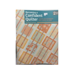May include: A book titled "Becoming a Confident Quilter" by Elizabeth Dackson. The book cover features a patchwork quilt design in shades of orange, yellow, and blue.