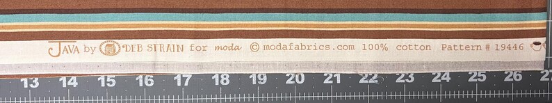 May include: Fabric sample with brown, teal, and beige horizontal stripes. The text "JAVA by DEB STRAIN for moda" is printed on a white strip, along with other details. The fabric is 100% cotton.