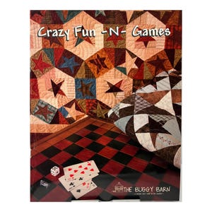 May include: A quilt pattern book titled Crazy Fun-N-Games by The Buggy Barn. The cover features a star-patterned quilt in red, blue, and brown tones, a red and black checkered game board, a single white die, and a small stack of playing cards.