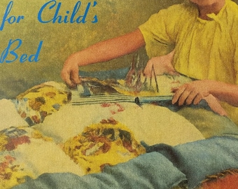 May include: A vintage image showing a child's bed with a patchwork quilt. The quilt has yellow, blue, and orange sections with floral patterns. The text in blue reads "Easily Made Eiderdown for Child's Bed."