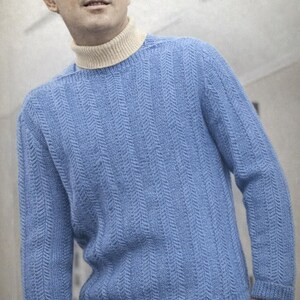 May include: A light blue sweater with a cream-colored turtleneck. The sweater has a textured, vertical pattern. The sleeves are long, and the cuffs are ribbed. The person is wearing beige pants.