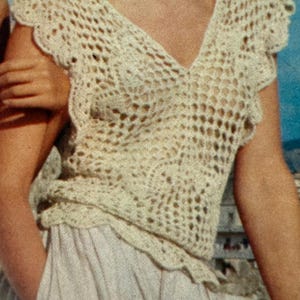 Puede incluir: Top de crochet color crema con cuello en V y bordes festoneados. El diseño de tejido abierto revela un vistazo a la piel del usuario. El top se combina con una falda de color claro, creando un aspecto suave y texturizado. También se ve un delicado collar.
