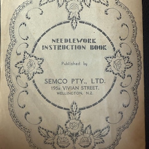 Puede incluir: Un libro de instrucciones de costura antiguo con un borde floral decorativo. La portada presenta el texto "NEEDLEWORK INSTRUCTION BOOK" y los detalles del editor: SEMCO PTY., LTD., 195a VIVIAN STREET, WELLINGTON, N.Z. El diseño es en tinta negra sobre fondo beige.