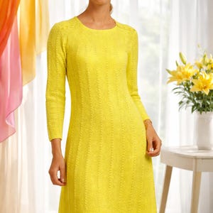 May include: A woman wearing a bright yellow, long-sleeved dress with a textured knit pattern. She is also wearing a brown hat with floral accents and gold earrings. A bouquet of yellow flowers sits on a small white table.