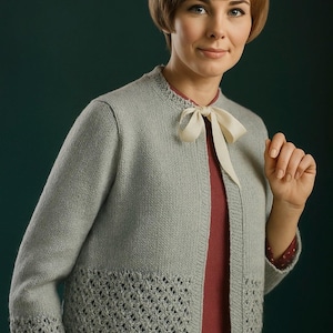 Peut inclure: Un cardigan en tricot gris clair avec un col rond et un nœud crème. Le cardigan présente un motif ajouré décoratif à l'ourlet et aux poignets. La femme porte un haut rouge en dessous.