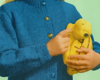 May include: A blue knitted cardigan with gold buttons. The cardigan is worn by a person holding a yellow stuffed animal. The stuffed animal has a black nose and is wearing a yellow outfit. The background is a solid green colour.