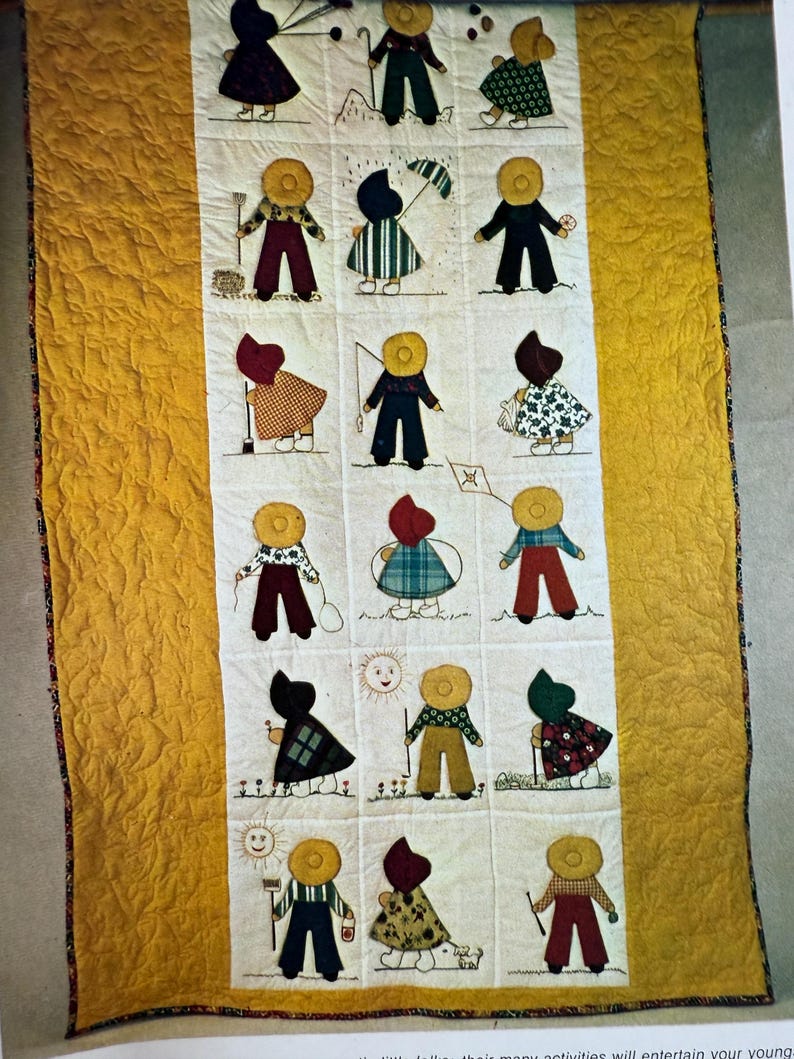 Puede incluir: Colcha hecha a mano con figuras aplicadas en varios atuendos, cada una con un sombrero amarillo. Las figuras est&aacute;n dispuestas en una cuadr&iacute;cula sobre un fondo blanco, bordeada por una tela amarilla texturizada. La colcha muestra un estilo de arte popular.