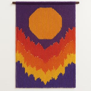 May include: A woven wall hanging with a geometric design. The artwork features a large orange sun shape against a purple background. Below the sun, a layered mountain range design transitions from yellow to orange to red.