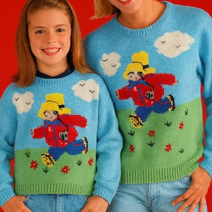 Könnte beinhalten: Zwei hellblaue Pullover mit einem Cartoon-Motiv einer rennenden Figur in einer roten Jacke und einem gelben Hut. Die Pullover haben einen grünen unteren Bereich mit Blumen und Wolken. Die Personen tragen blaue Jeans.