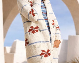 May include: Cream-coloured, long cardigan sweater with blue stripes and red floral embroidery. The sweater has a hood, pockets, and button closures. The person is wearing a blue and white striped shirt and blue trousers.